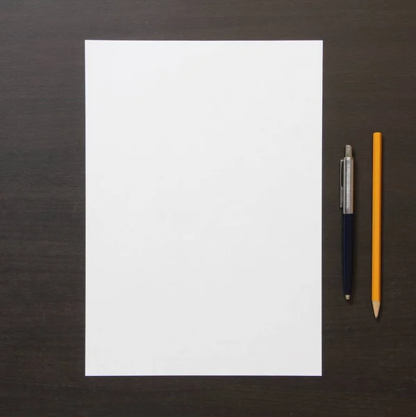 Szablon białego papieru z piórem i ołówkiem na ciemnym wenge kolor drewniane tło. — Zdjęcie stockowe