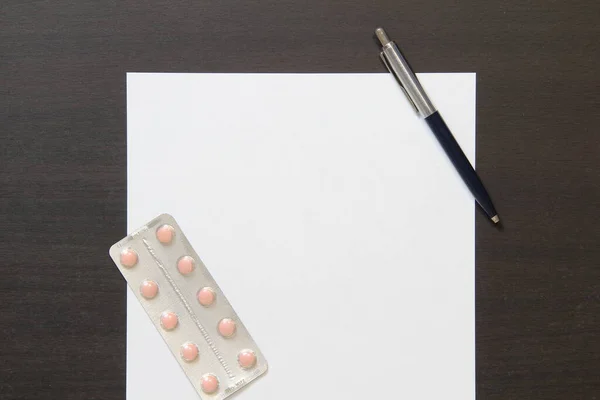 Modelo de papel branco com caneta e pílulas em uma bolha no fundo de madeira cor wenge escuro . — Fotografia de Stock