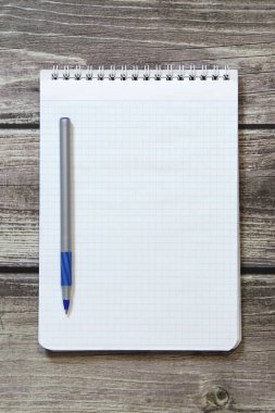 Notepad with a blank white sheet in a checker paper with ball pen lies on the background of wooden boards
