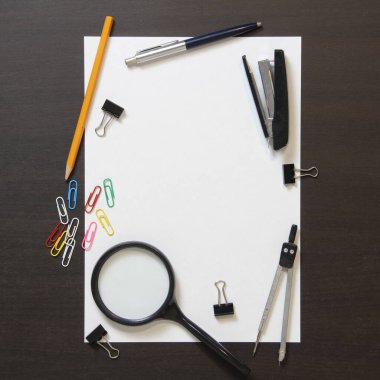 Beyaz kağıt şablonu kalem, büyüteç, zımba, ataç ve koyu renkli ahşap zemin üzerine diğer kırtasiye malzemeleri. Metin için boş alanı olan stok fotoğrafı 