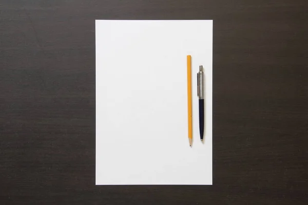 Szablon białego papieru z piórem i ołówkiem na ciemnym wenge kolor drewniane tło. — Zdjęcie stockowe