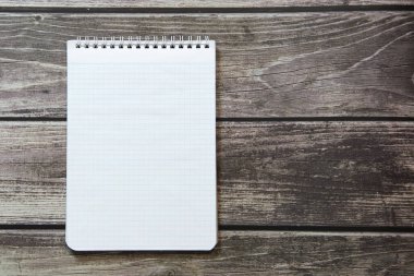 Tahta tabloların arka planında duran boş beyaz sayfalı bir not defteri.