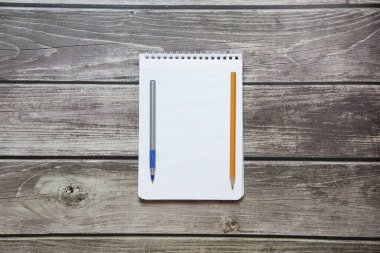 Tahta panoların arka planında taşlı kalem ve basit grafit kalemle dolu boş beyaz bir sayfa olan not defteri var..