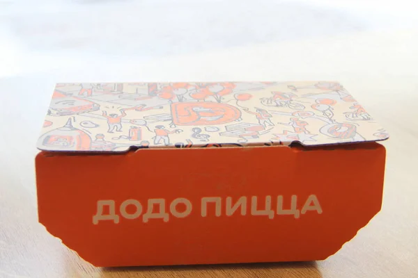 2020 ロシア Syktyvkar サイド碑文のピザとDodoスナック用オレンジ段ボール箱と蓋の企業デザインとロゴが窓の近くのレストランのテーブルの上に立っています — ストック写真