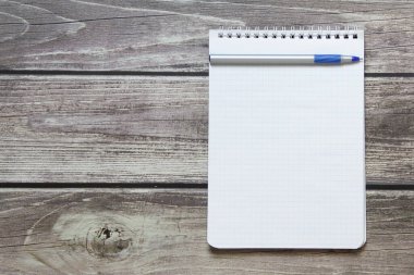 Notepad with a blank white sheet in a checker paper with ball pen lies on the background of wooden boards.