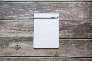 Notepad with a blank white sheet in a checker paper with ball pen lies on the background of wooden boards.