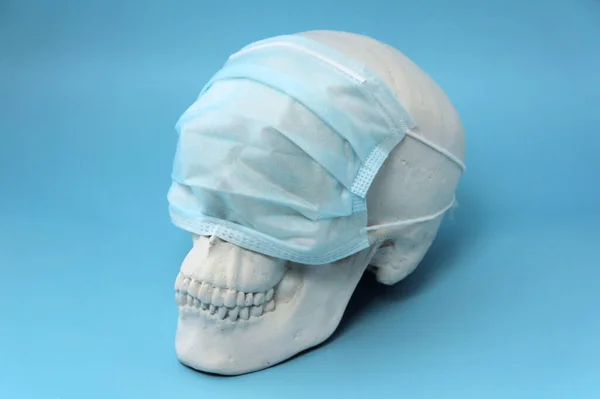 青い背景に石膏で作られた白い人間の頭蓋骨で 彼の目には医療マスクが付いています 流行およびコロノウイルスの概念 — ストック写真
