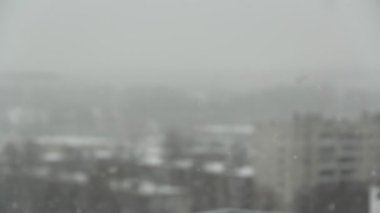 Şehrin arka planında kar yağışı. Gri gökyüzünden kar yağıyor, kar taneleri ön planda uçuyor..