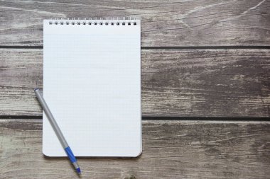 Notepad with a blank white sheet in a checker paper with ball pen lies on the background of wooden boards.