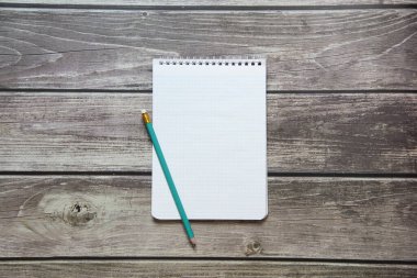 Tahta panoların arka planında basit grafit kalemle işaretleyici kağıdında boş beyaz bir sayfa bulunan bir not defteri var.