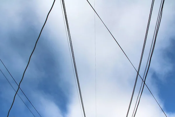 Interweaving of wires and cables against the blue sky with clouds. Industrial city landscape.