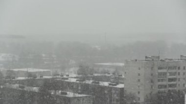 Şehrin arka planında kar yağışı. Gri gökyüzünden kar yağıyor, kar taneleri ön planda uçuyor.