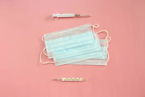 ピンクの背景に医療使い捨てマスク、温度計、注射器。コロノウイルス発生防衛コンセプト — ストック写真