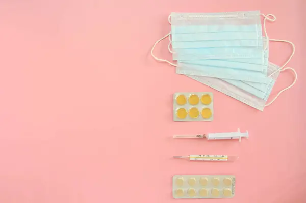 Medyczne jednorazowe maski, termometr, strzykawka i tabletki na różowym tle. Koncepcja obrony przed epidemią koronowirusa — Zdjęcie stockowe
