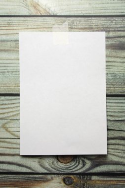 Tahta bir arka planda bir parça bant yapıştırılmış beyaz bir A4 kağıdı duvara asılmış.