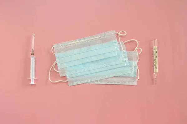 Medyczne jednorazowe maski, termometr i strzykawka na różowym tle. Koncepcja obrony przed epidemią koronowirusa — Zdjęcie stockowe