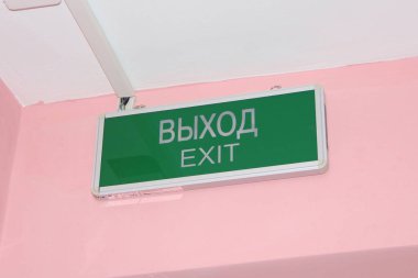 Üzerinde İngilizce ve Rusça yazılar olan yeşil levha pembe bir duvarda.