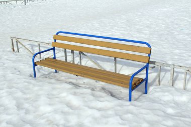 Karlı zeminde metal mavi tabanlı ahşap bir bankta.