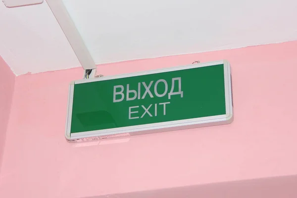 Placa verde com a saída de inscrição em inglês e russo em uma parede rosa — Fotografia de Stock