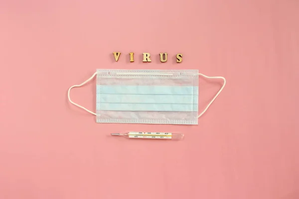 医療使い捨てマスク、温度計、ピンクの背景にコロウイルスという言葉を形成する木製の手紙 — ストック写真