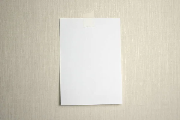 An einer Wand hängt ein weißes Blatt Papier, das mit einem Stück Klebeband auf hellem Hintergrund beklebt ist. — Stockfoto