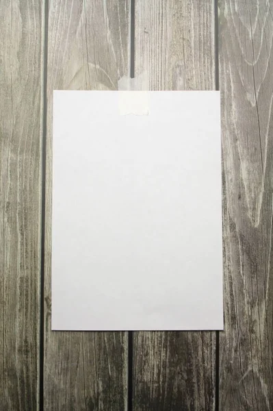 A white sheet of A4 paper hanging on a wall glued with a piece of paper tape on a wooden background — Stock Photo, Image