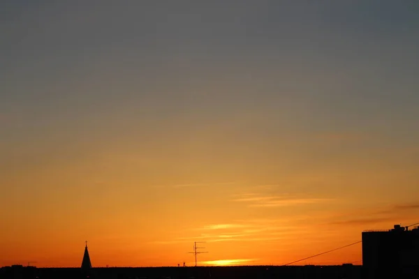 Sun below the horizon and the roof of the church with a cross, television antenna in the background fiery dramatic orange sky at sunset or dawn backlit by the sun. Place for text and design