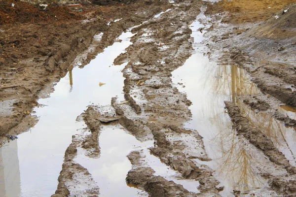 Strada sterrata sporca con pista, segni di ruote, argilla marrone e pozzanghere in Russia — Foto Stock