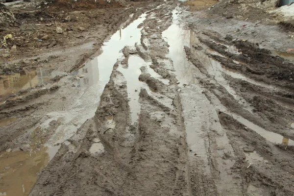 俄罗斯肮脏的土路，有铁轨、车轮痕迹、褐色粘土和水坑 — 图库照片
