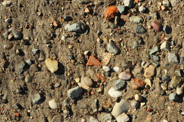 Malé kameny a písek. Přirozená struktura půdy. Pobřeží přehrady s pláží a oblázky — Stock fotografie