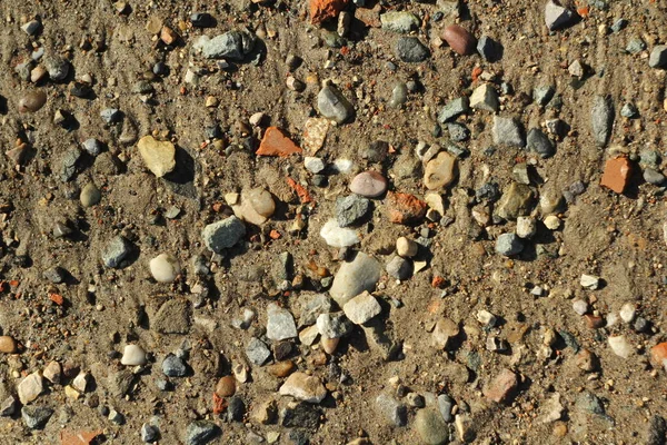 Små stenar och sand. Jordens naturliga struktur. Stranden av en reservoar med en strand och småsten — Stockfoto