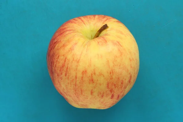 Czerwone żółte jabłko na niebieskim tle. Soczyste dojrzałe piękne owoce — Zdjęcie stockowe