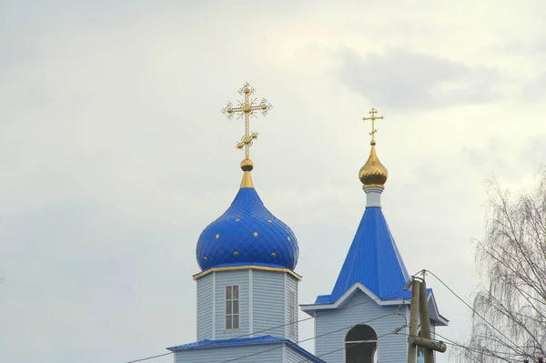 Православная христианская церковь с белыми стенами, голубыми куполами и золотыми крестами в России. Здание для религиозных церемоний с колокольней на фоне облачного неба в сельской местности — стоковое фото