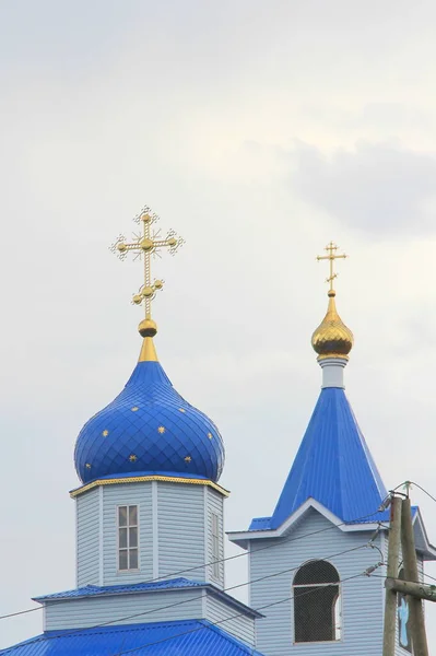 Iglesia ortodoxa cristiana con paredes blancas, cúpulas azules y cruces doradas en Rusia. Un edificio para ceremonias religiosas con un campanario contra un cielo nublado en el campo — Foto de Stock