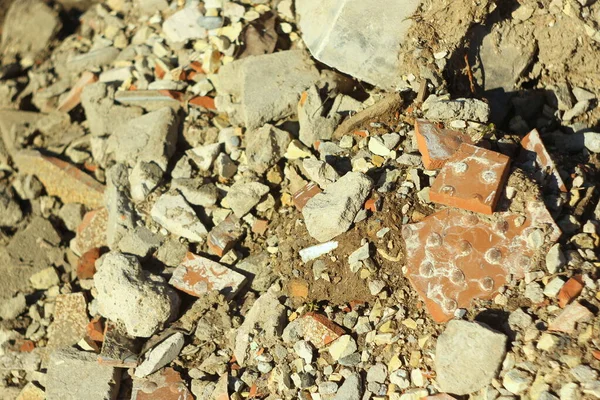 A Una dispersión de piedras, tierra, arena, fragmentos de azulejo y hormigón. Piezas de cemento y residuos de construcción por la tarde a la luz del sol. Fondo para texto, diseño, patrón y fondo de pantalla — Foto de Stock