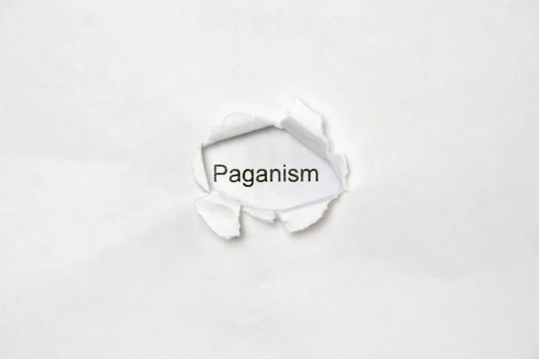 Слово Паганізм на білому ізольованому тлі через отвір рани в папері . — стокове фото