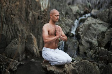 Budist. Kel adam. Bir şelalenin arka planına karşı dağlarda meditasyon. Dua et..
