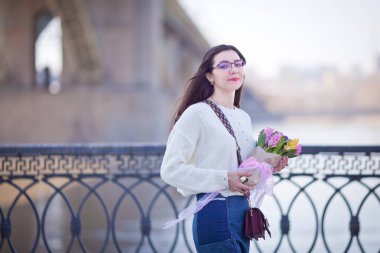 Güzel bir kız elinde bir buket bahar çiçeğiyle gezinti güvertesinde yürüyor, bir buket sümbül.
