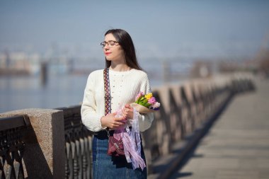 Güzel bir kız elinde bir buket bahar çiçeğiyle gezinti güvertesinde yürüyor, bir buket sümbül.