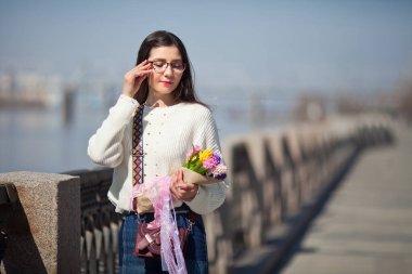 Güzel bir kız elinde bir buket bahar çiçeğiyle gezinti güvertesinde yürüyor, bir buket sümbül.