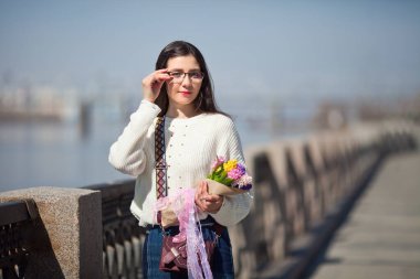 Güzel bir kız elinde bir buket bahar çiçeğiyle gezinti güvertesinde yürüyor, bir buket sümbül.