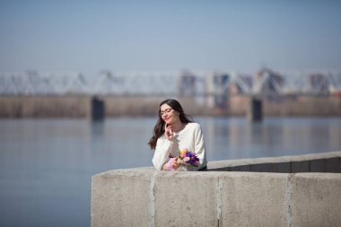 Güzel bir kız elinde bir buket bahar çiçeğiyle gezinti güvertesinde yürüyor, bir buket sümbül.