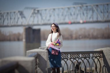Güzel bir kız elinde bir buket bahar çiçeğiyle gezinti güvertesinde yürüyor, bir buket sümbül.