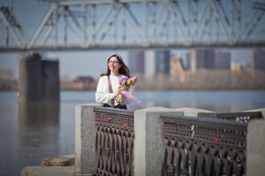 Güzel bir kız elinde bir buket bahar çiçeğiyle gezinti güvertesinde yürüyor, bir buket sümbül.