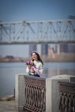 Güzel bir kız elinde bir buket bahar çiçeğiyle gezinti güvertesinde yürüyor, bir buket sümbül.