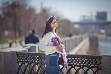 Güzel bir kız elinde bir buket bahar çiçeğiyle gezinti güvertesinde yürüyor, bir buket sümbül.