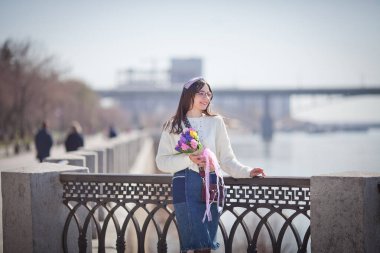 Güzel bir kız elinde bir buket bahar çiçeğiyle gezinti güvertesinde yürüyor, bir buket sümbül.