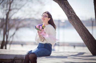 Güzel bir kız elinde bir buket bahar çiçeğiyle gezinti güvertesinde yürüyor, bir buket sümbül.