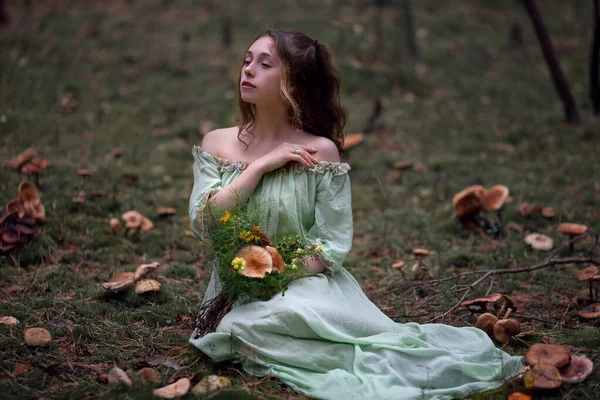 魔法の森の妖精についてのおとぎ話緑のドレスの美しい少女が花束を持って森の中を歩きます — ストック写真