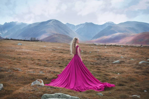 Fairy tale. A girl in a pink dress with a long train walks on a background of mountains.